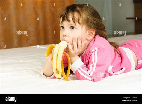 Cute Little Girl Eating A Banana On The Bed At Home Stock Photo Alamy