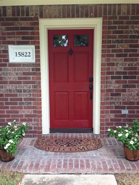 A Red Front Door With Two Planters On The Side And A Brick Walkway