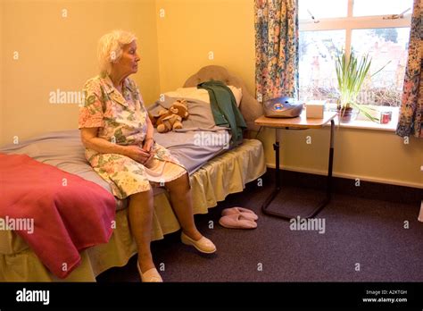Lonely Old Lady In Nursing Home Sitting On Edge Of Bed Lookig Out Of