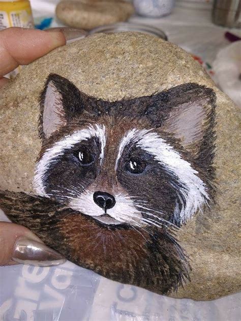 A Hand Holding A Rock With A Painting Of A Raccoon Painted On It