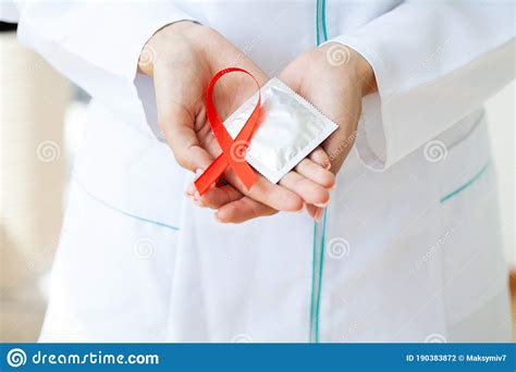 Doctor Holding A Red Ribbon And Condom Calling For Safe Sex And