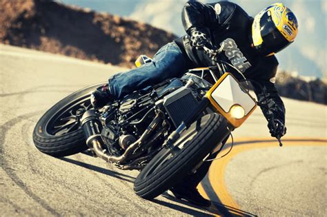 A Man Riding On The Back Of A Motorcycle Down A Curvy Road