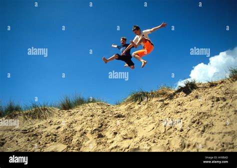 Two Boys Jumping Over Sand Dunes Camber Sands East Sussex Uk Stock