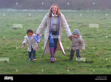 A Mother And Two Young Children Holding Hands And Running Through The