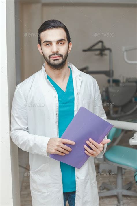 a man in a white lab coat is holding a binder and looking at the camera
