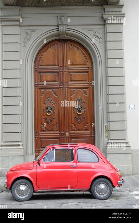 Red Fiat 500 Parked On The Street In Front Of An Old Brown Wood