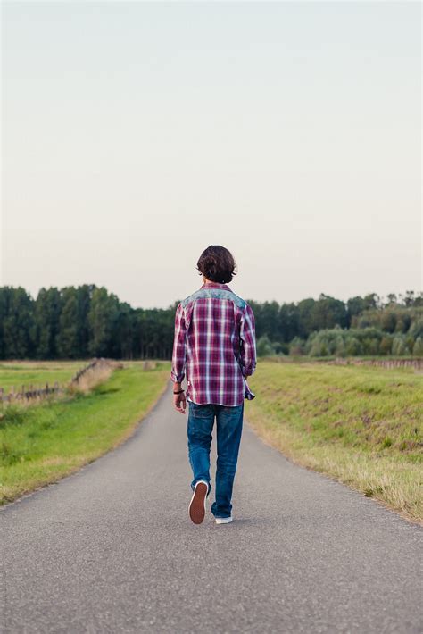 Teenage Boy Walking Away On A Long Road In The Fields Del Colaborador