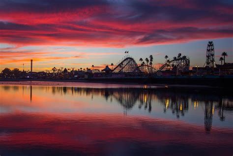 An Amusement Park At Sunset With The Sky Reflected In The Water And
