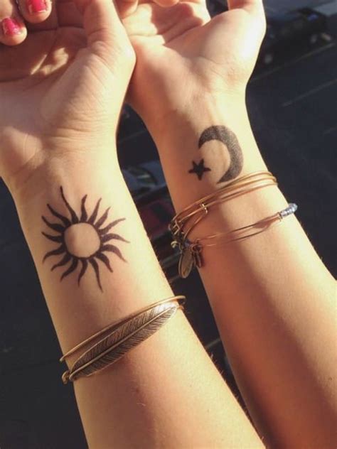 Two People Holding Hands With Tattoos On Their Wrists And The Sun And