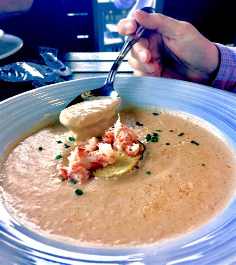 A Person Holding A Spoon Over A Bowl Of Soup With Shrimp And Cream In It