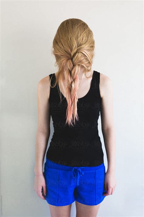 teen girl hides behind hair that she has plaited in front of her face by stocksy contributor
