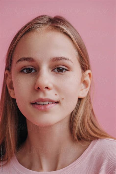 headshot natural beauty portrait of teen gently smiling against pink background beauty portrait