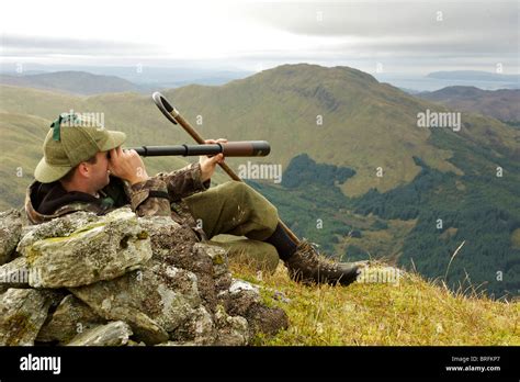 Scottish Deer Stalker On Top Of A Mountain Spying For Deer Using A