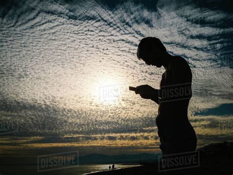 Silhouette Of Man With Naked Torso Using Smartphone On Background Of