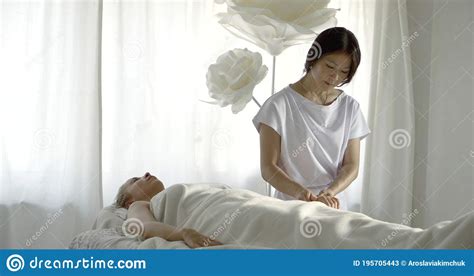 Asian Masseuse Is Stroking Fingers Arm And Head Of Relaxed Female Client Lying On Table Stock