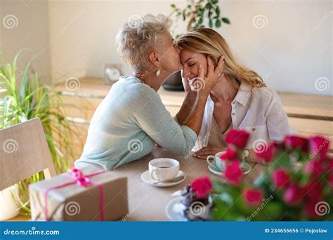 lycklig äldre mor som har kaffe med vuxen dotter inomhus hemma och kysser henne på pannan