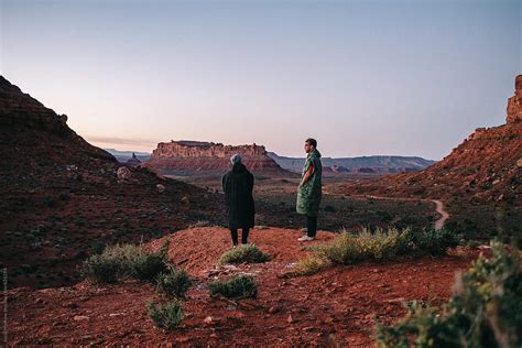 Two Young Men Stand On Edge Of Cliff During Sunrise In Sandstone