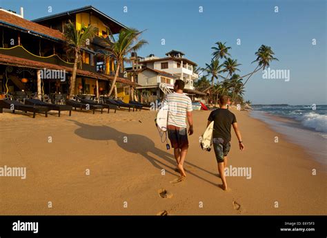 Two Male Surfers Carrying Their Boards On The Beach At Hikkaduwa Sri