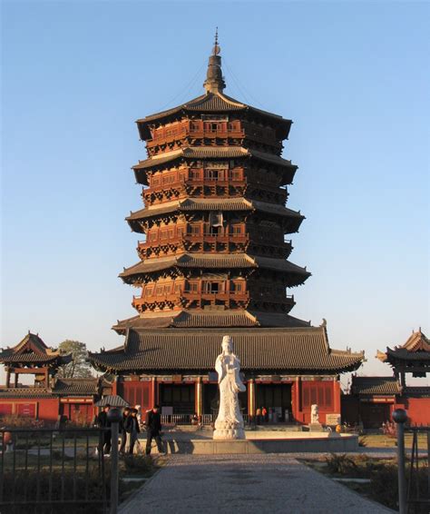 A Tall Tower With Statues In Front Of It And People Walking Around The