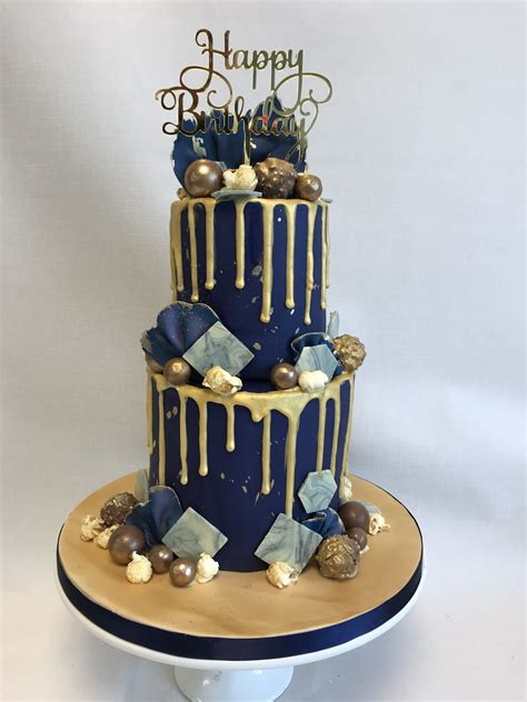 A Three Tiered Blue And Gold Birthday Cake With White Icing Dripping