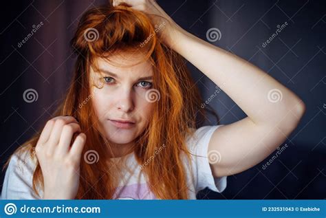 Young Red Haired Girl Touches Her Tousled Hair And Looks At Camera