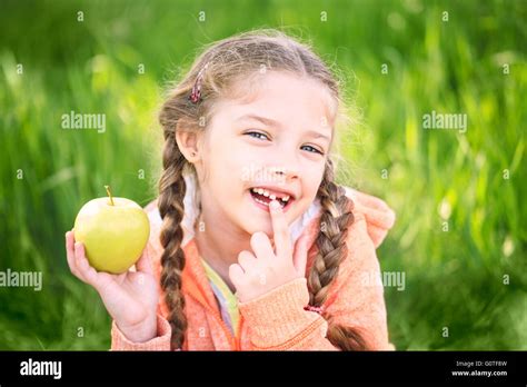 Sweet Girl With A Fallen Toth Holding An Apple In Her Hand On Nature