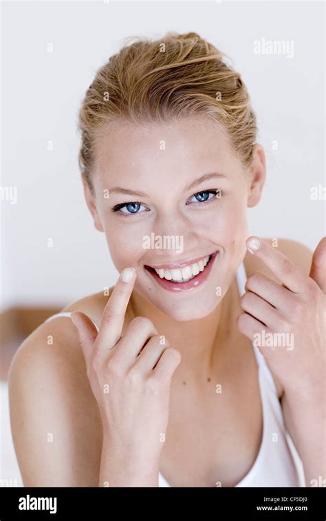 Female Fair Hair Off Her Face Wearing A White Vest Black Eyeliner Glossy Lips Applying Face