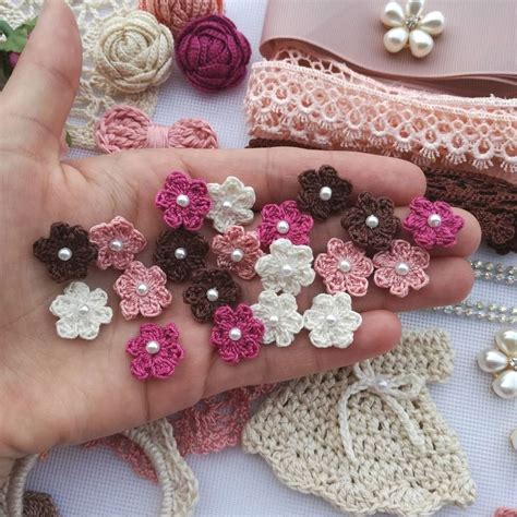 A Hand Holding Several Small Crocheted Flowers In Its Palm Surrounded