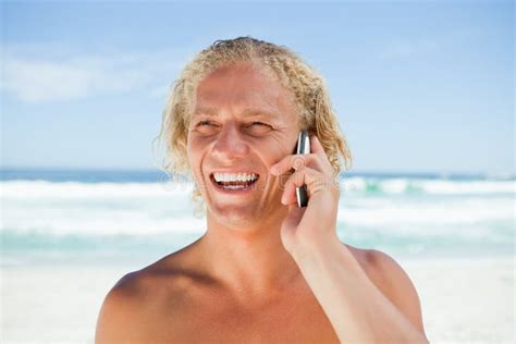 Smiling Man Using His Mobile Phone While Standing On The Beach Stock