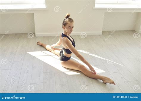 Concentrated Young Woman Doing Forward Split On Floor In Gym Or Modern