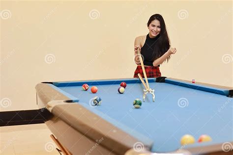 beautiful and asian woman in black dress playing billiard or snooker on blue pool table with