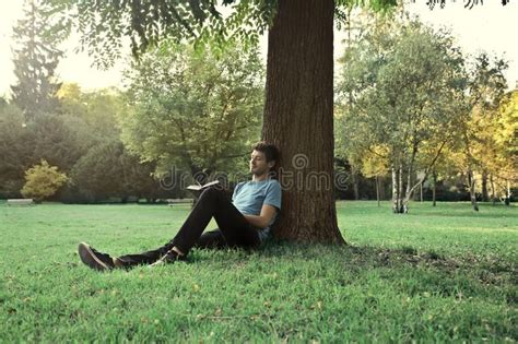Spare Time Young Man Sitting Under A Tree In A Park And Reading A Book