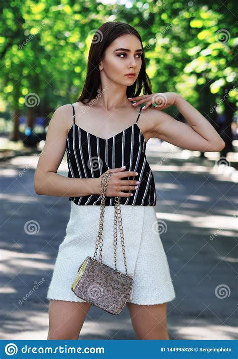 Young Girl Model Posing At The Park Looking Left And Keeping A Bag