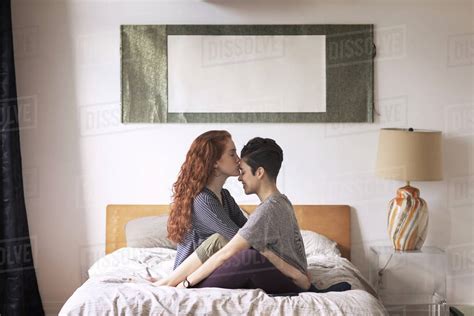 Romantic Lesbian Kissing On Girlfriend S Forehead While Sitting On Bed At Home Stock Photo