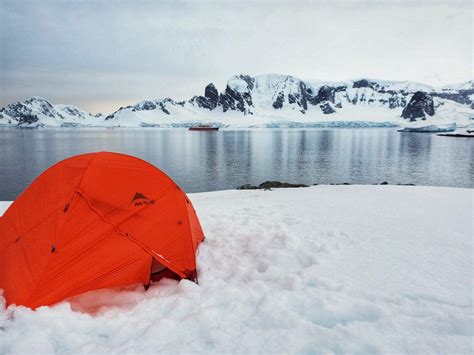 An Orange Tent Sitting On Top Of Snow Covered Ground Next To The Ocean
