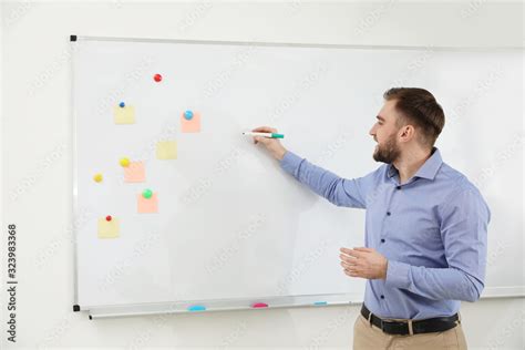 Portrait Of Young Teacher Writing On Whiteboard In Classroom Stock