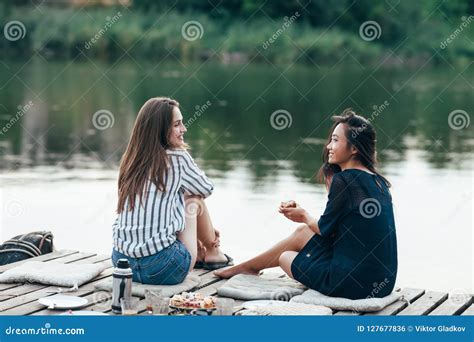 Two Female Friends Talking At A Pier Relaxing On Lake Stock Photo