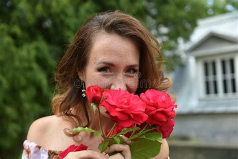 Beautiful Brunette Woman With Red Roses Near The Bush In The Park Stock