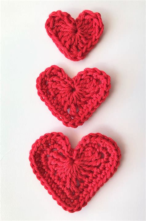 Two Crocheted Hearts Sitting Next To Each Other On Top Of A White Surface