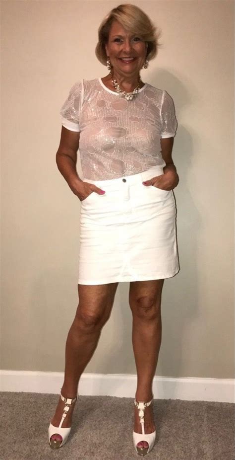 a woman standing in front of a wall wearing a white skirt and sheer shirt with her hands on her hips
