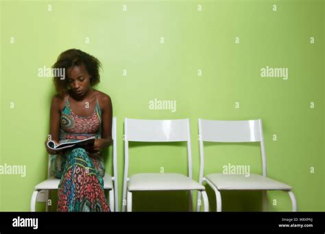 Beautiful African American Woman Sitting On Chair And Reading Magazine In Waiting Room Of