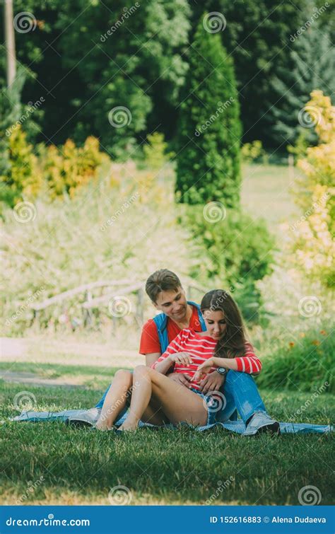 Young Loving Couple Is Sitting On A Plaid In The Park Hugging Fooling