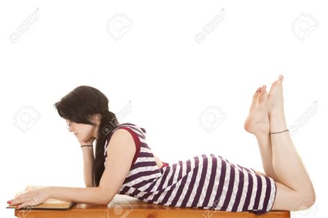 A Woman Laying On Her Stomach Reading With Her Bare Feet Up Stock