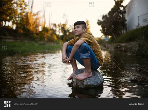 Boy Sitting Barefoot On Rock In A Stream Stock Photo Offset