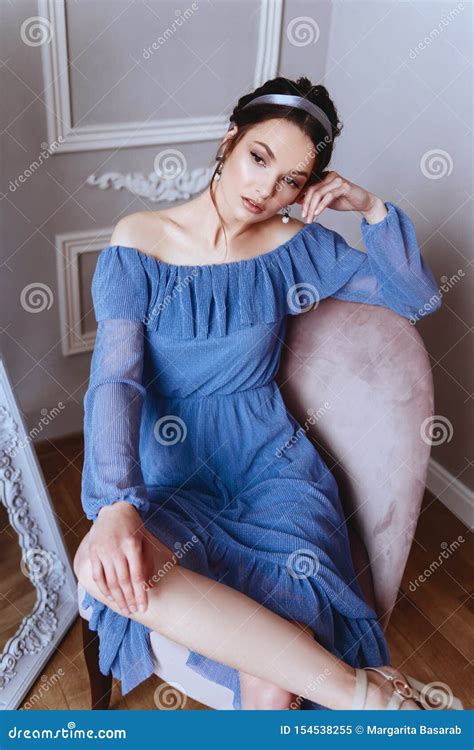 A Beautiful Woman In A Blue Dress Is Sitting On A Velvet Armchair Stock