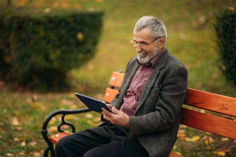 Grandpa Uses A Tablet Sitting In The Park On The Bench Stock Image