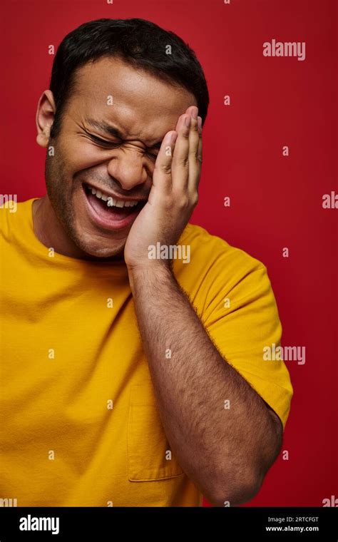 face expression embarrassed indian man in yellow t shirt laughing and touching face on red