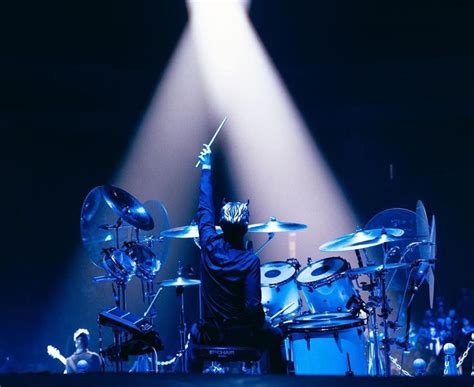 A Man With His Arms Up In The Air While Playing Drums On Stage At A Concert