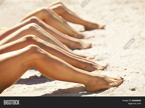 Legs Of Several Girls Lying On Sandy Beach And Tanning In The Bright