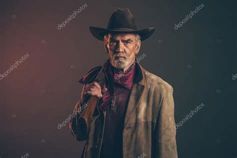 Old Rough Western Cowboy With Gray Beard And Brown Hat Holding R